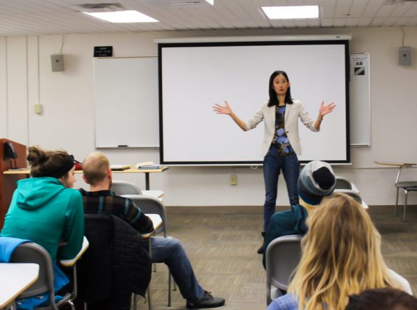Professor gestures with her hands at the front of a classroom full of students