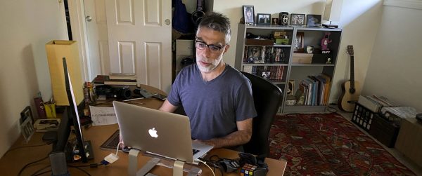 Man sits at desk behind a laptop computer in a home office.