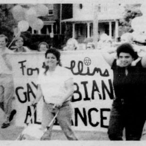 Black-and-white photo of young people marching with balloons and a sign that reads "Fort Collins Gay/Lesbian Alliance"