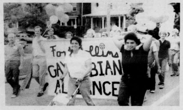 Black-and-white photo of young people marching with balloons and a sign that reads "Fort Collins Gay/Lesbian Alliance"