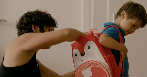 Parent helps toddler put on a backpack that looks like a fox