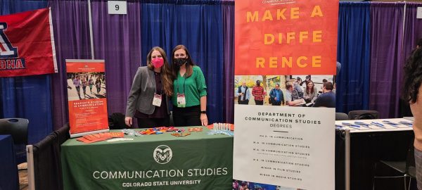 Two women wearing face masks standing behind their table at a conference fair