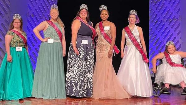 Pageant contenders line up on stage in ballgowns, crowns, and sashes