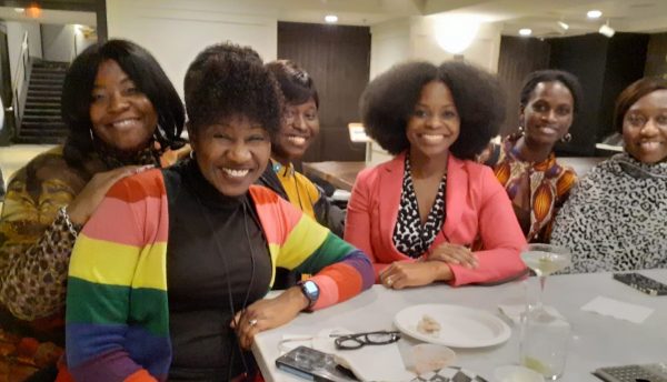 Six Black women smile together around a table