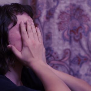 Scene from a student short film: woman on sofa with hands covering her eyes.