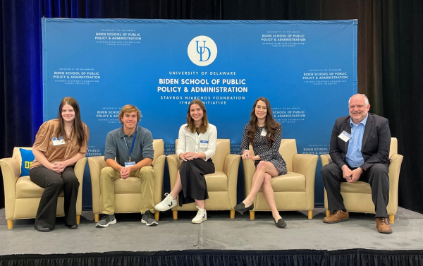 Four students and professor sit on stage with "University of Delaware Biden School of Public Policy & Administration Stavros Niarchos Foundation Ithaca Initiative" backdrop behind them