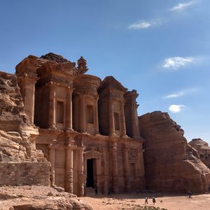 Photo of Petra, Jordan--an ancient building facade carved out of a red stone monolith, with a blue sky behind it