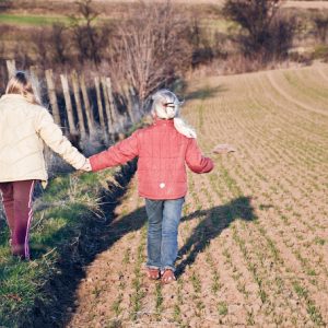 Two small children walking away while holding hands in a field.