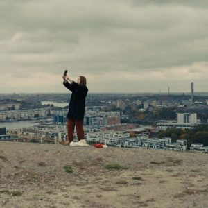 A woman stands in an open space holding a cell phone high into the air.