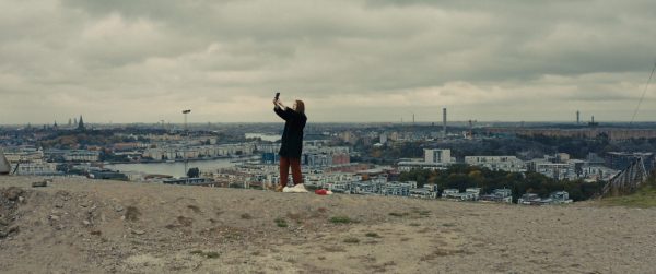 A woman stands in an open space holding a cell phone high into the air.