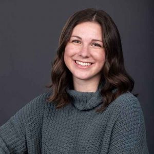 Photo of Olivia Birg in a grey sweater and jeans against a grey background