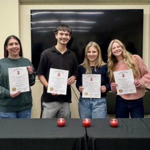 Four students hold their certificates for membership into Lambda Pi Eta