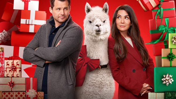 a movie promotional image featuring a man and a woman with a llama standing between them and surrounded by Christmas presents