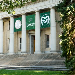 Front entrance of a historic building with "Go Green" banners and large columns surrounded by trees.
