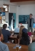 Before an audience, a man in a blazer speaks before a screen that reads "A liberal psychological complex." One wall of the room is lined with full bookshelves.